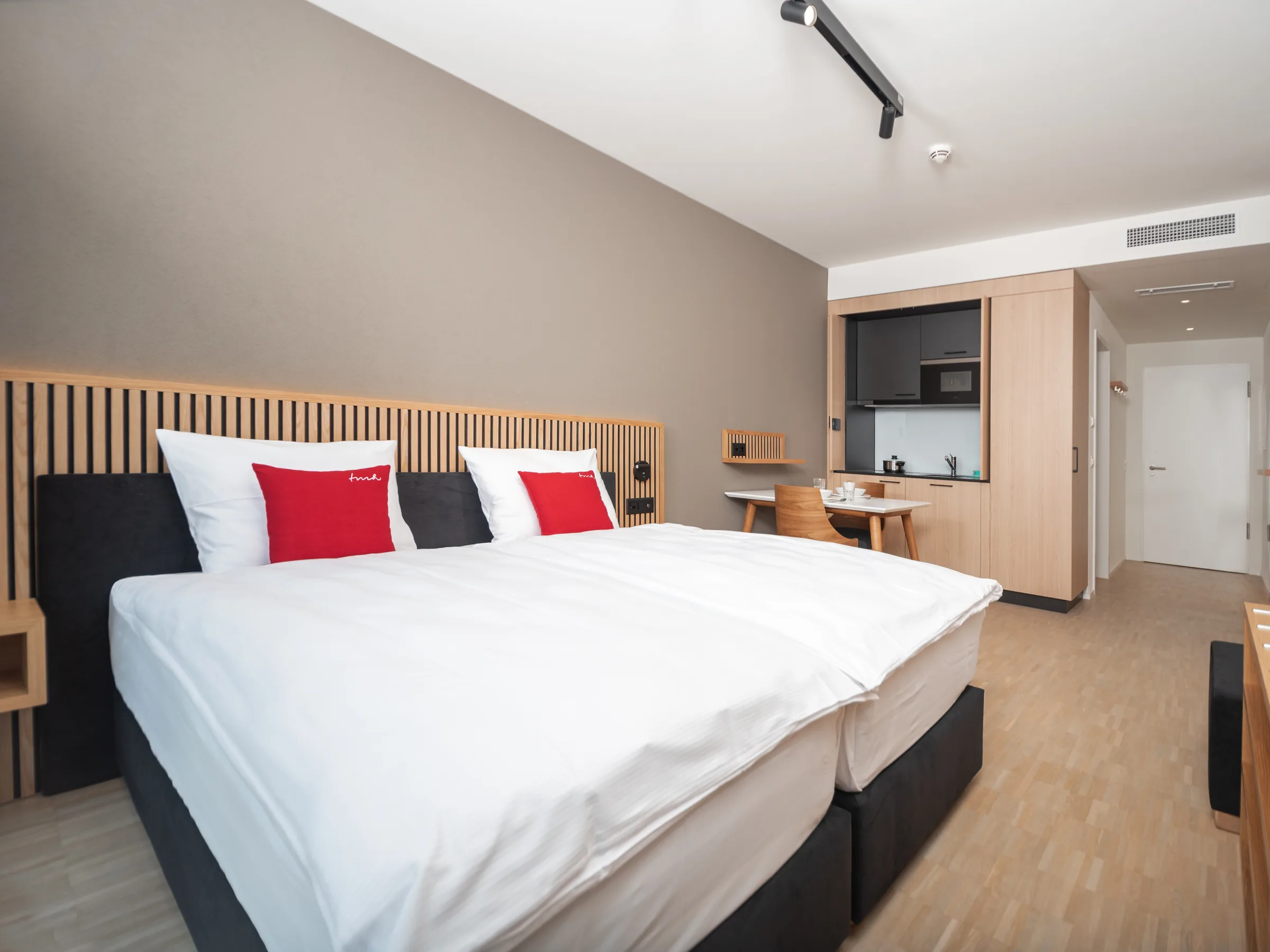 Zimmer im Hotel BAB in Bachenbülach mit Kopfteil aus Holzlatten, Doppelbett und Küchenzeile